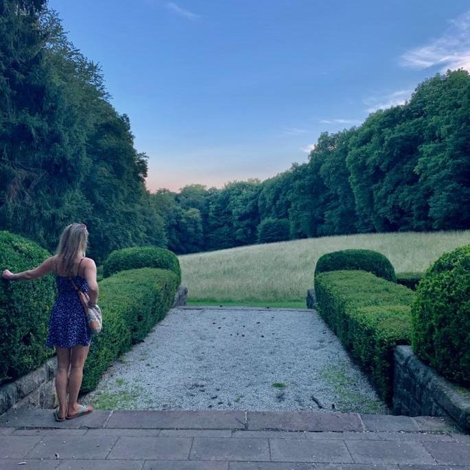 Lisa Sofie Zelgin steht an einer Hecke und schaut über eine weite Wiese